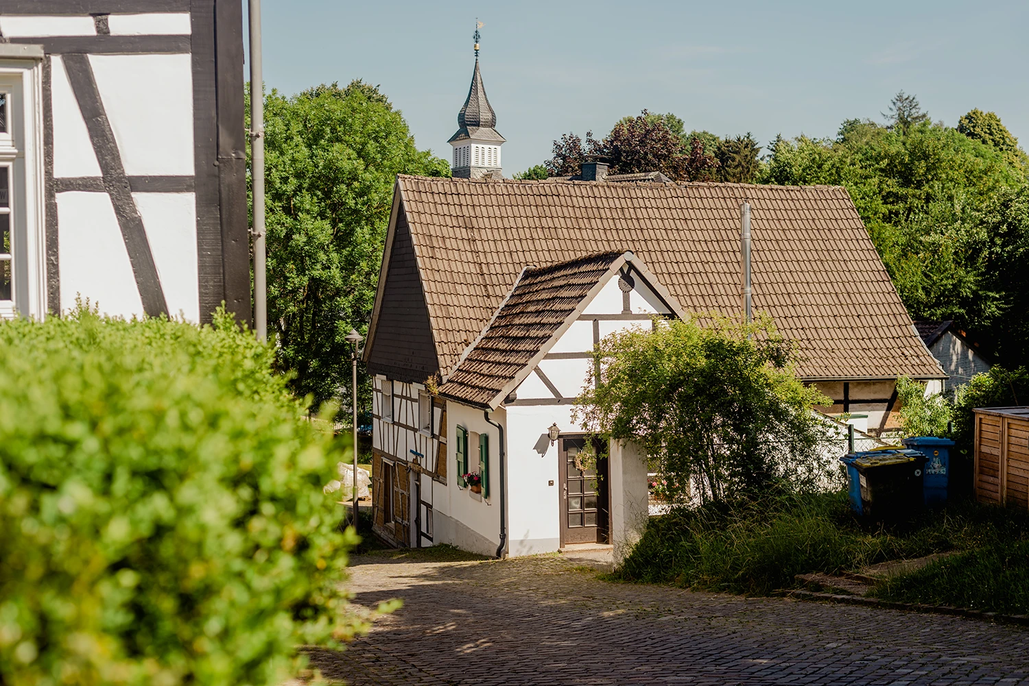 Altbau sanieren – traditionelles Fachwerkhaus mit Ziegeldach und Kirchturm im Hintergrund als typisches Bestandsgebäude