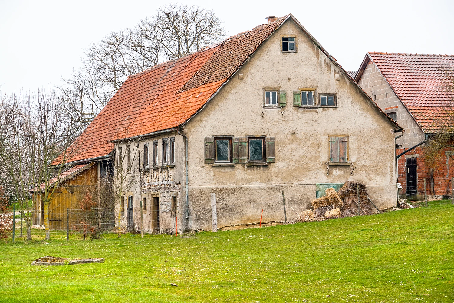 Älteres Einfamilienhaus als Sanierungsfall mit sichtbarem Sanierungsbedarf an Fassade und Dach – Symbol für die Entscheidung sanieren oder verkaufen