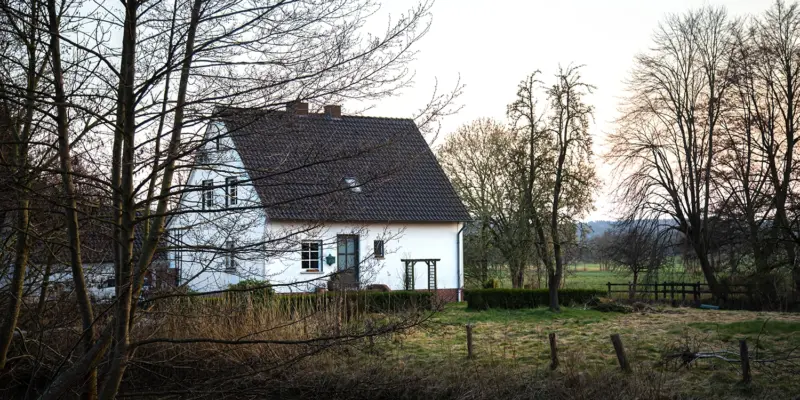 Älteres weißes Einfamilienhaus im ländlichen Umfeld – Entscheidungssituation für Eigentümer, ob sie sanieren oder verkaufen